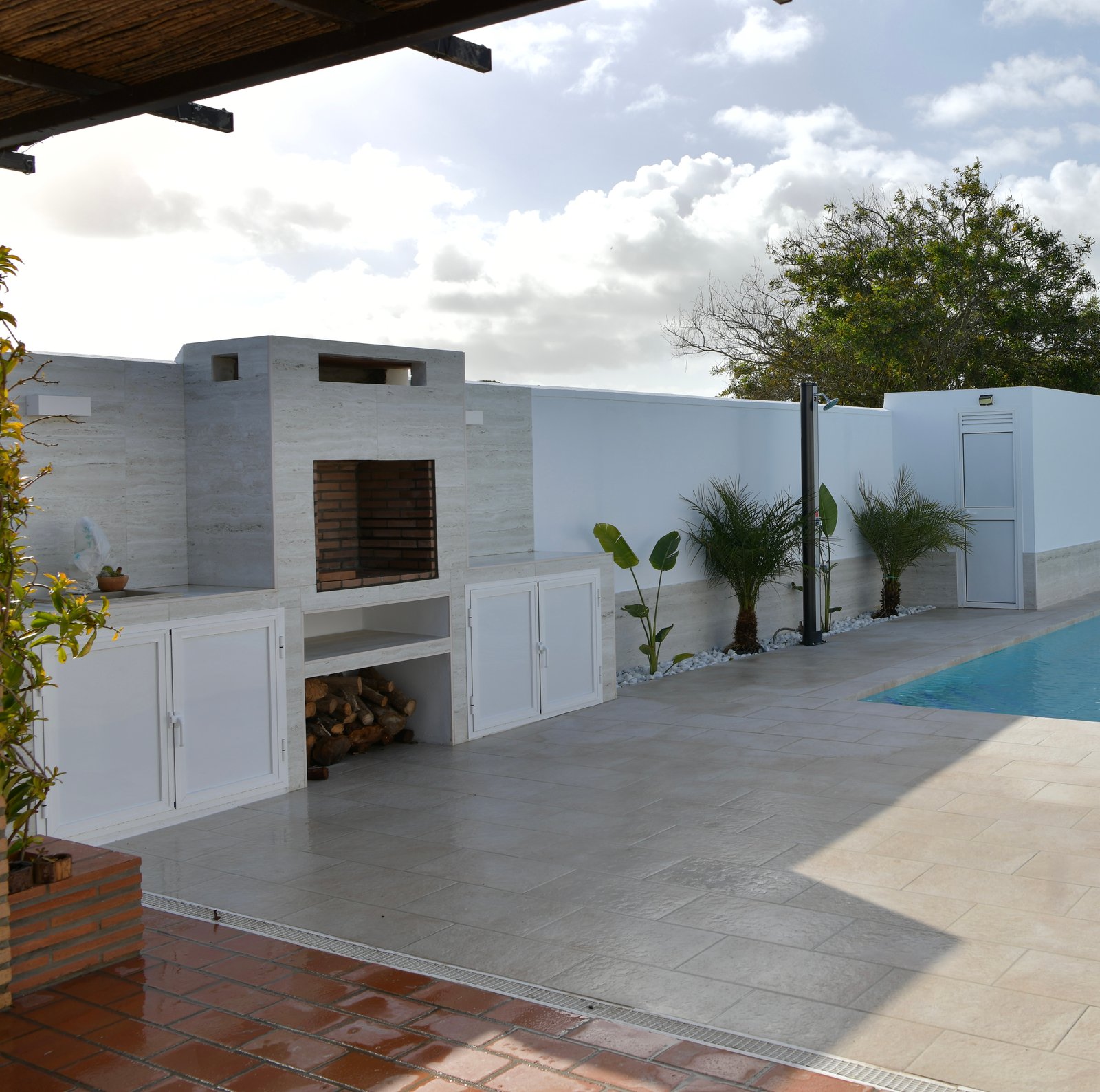 Nueva barbacoa moderna con leñero, armarios y zona de piscina.