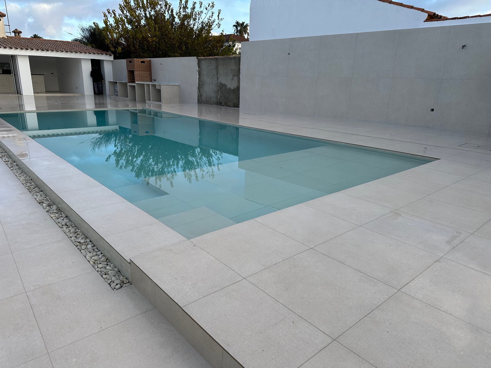Piscina llena con porcelánico claro y jardinera integrada